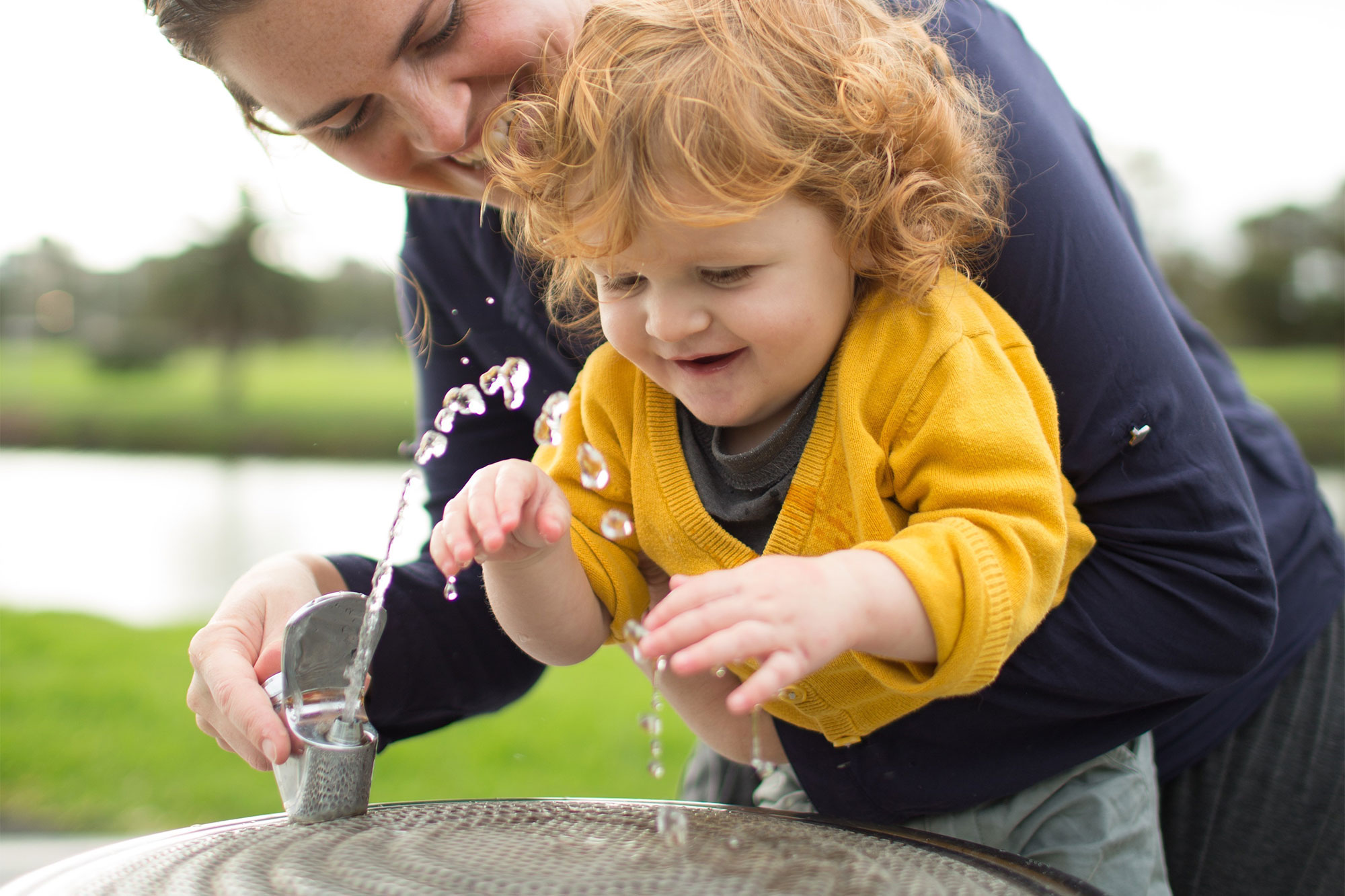 A woman and her child drink from a public water fountain