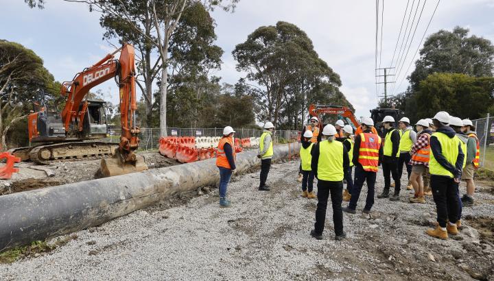 People in hi-vis vests stand in front of pipeline