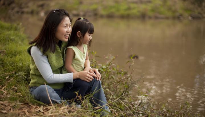 A woman and a child sit on the banks of a river