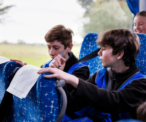 Two students on excursion bus filling out activity sheets