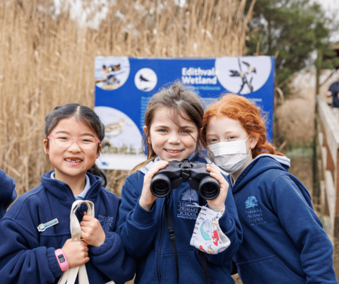 Three primary school girls looking into the camera and smiling out the front of the Edithvale Wetland sign