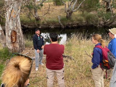 Ash Skinner stands delivers an education session by a waterway