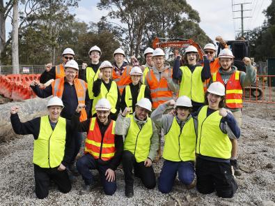 Swinburne TAFE students visit M55 Kilsyth to Croydon A group of people wearing hi-vis vests and hard hats fist pump the air at a construction site