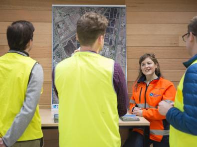 A group of 4 people wearing hi-vis PPE standing beside an aerial photo of a Melbourne Water facility