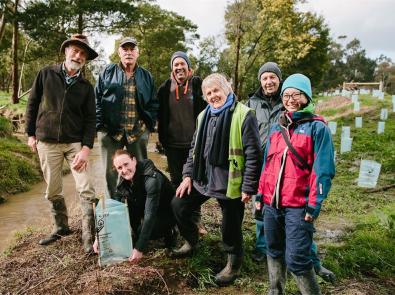 Group of people stand next to a waterway with freshly planted seedlings