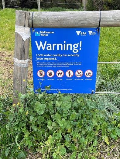 Blue warning sign attached to a gate, advising of impacts to water quality.