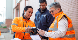 Three diverse people standing outside having a conversation over a device screen