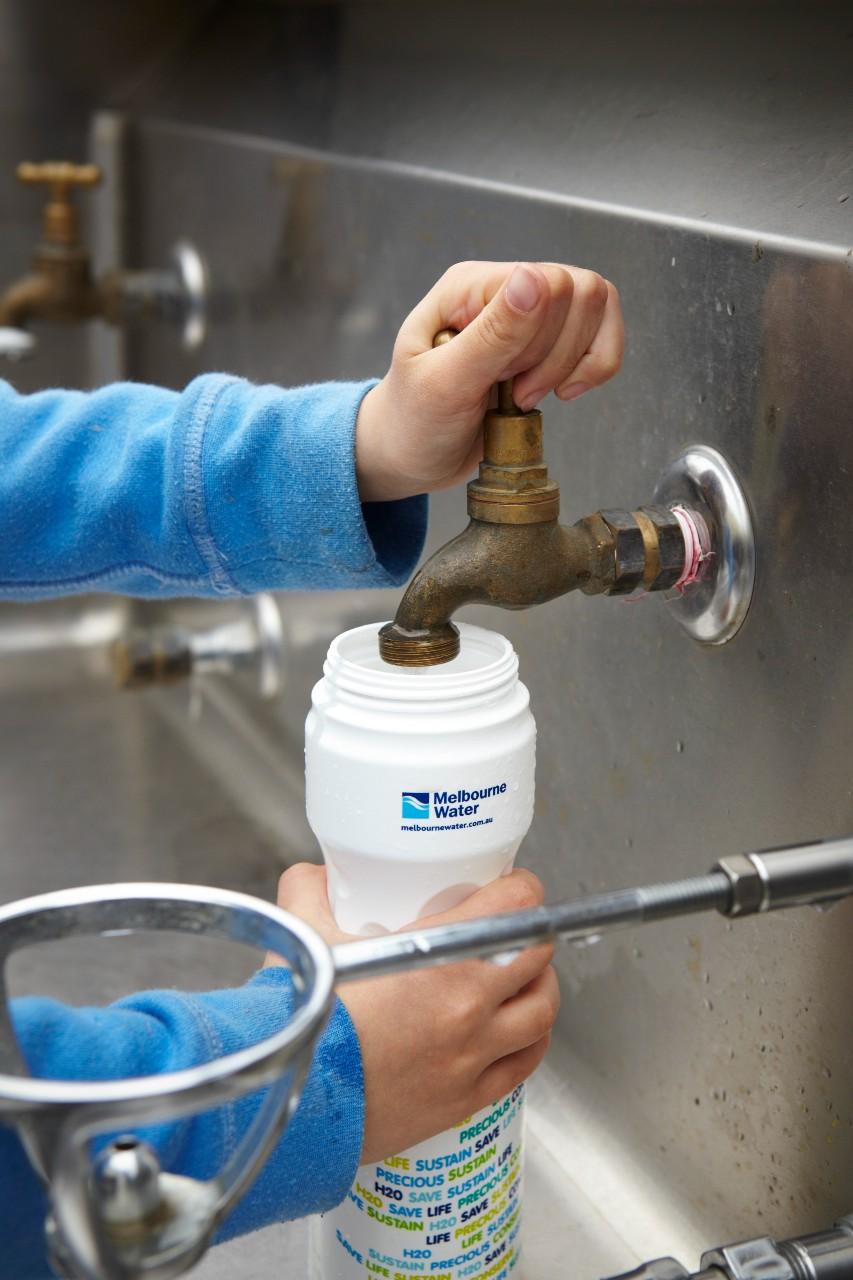 A young person fills up a Melbourne Water branded water bottle at a tap-resized