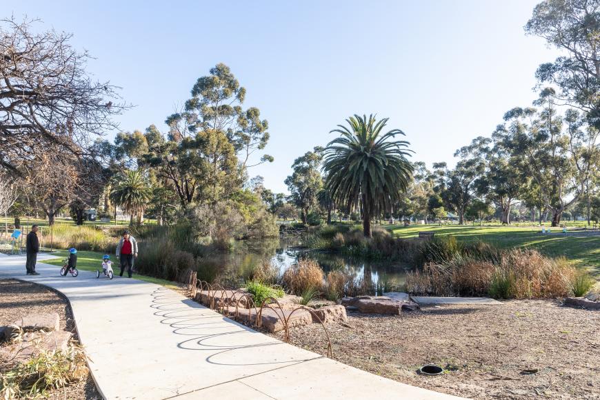 Family walking and cycling on a path alongside a wetland. Lawn and trees in background.