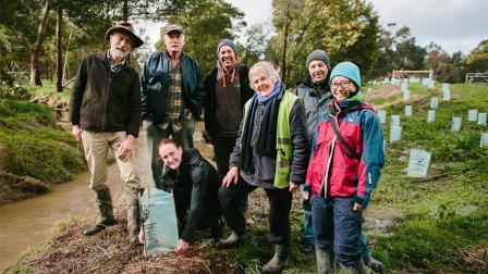 Group of people stand next to a waterway with freshly planted seedlings